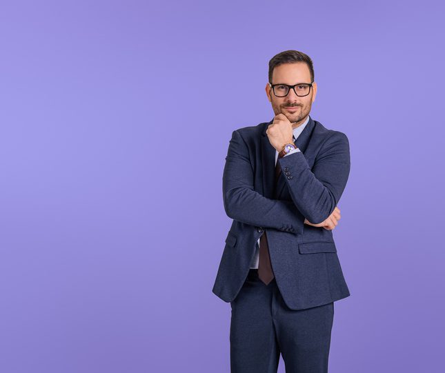 Confident businessman in a navy suit posing thoughtfully against a purple background.