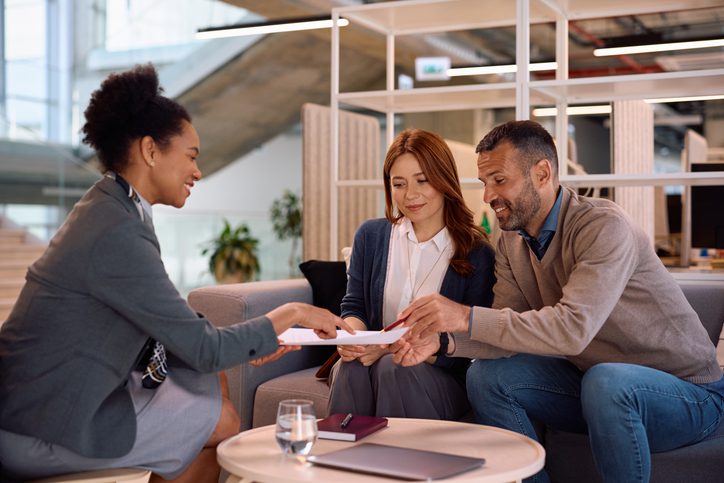 A couple reviewing documents with a woman in a modern office.