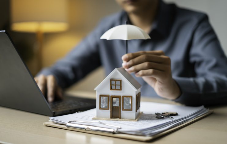Person holding an umbrella over a small house model on documents.